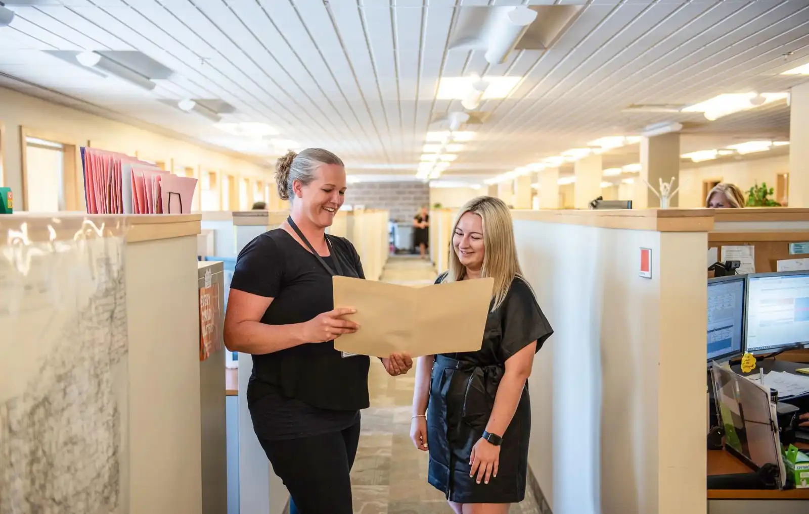 Two Community & Social Services staff chat with each other while reviewing documents in the hallway