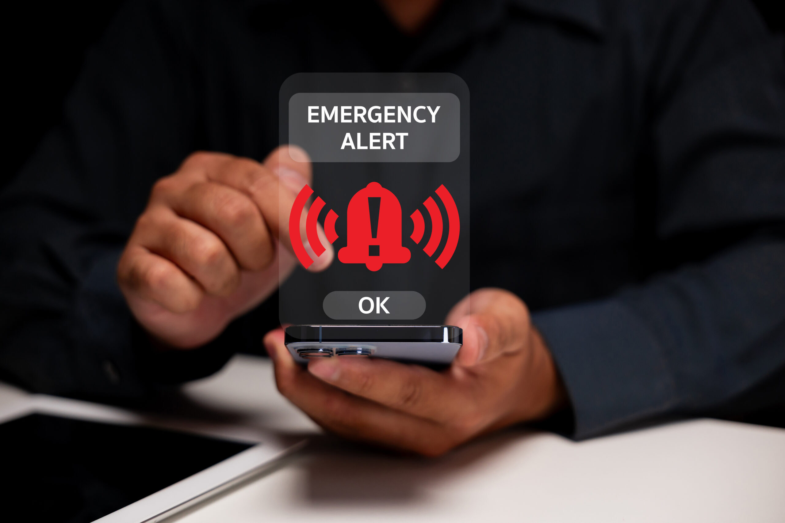 A person holding a smartphone with an emergency alert notification displayed on the screen, signaling urgent information.