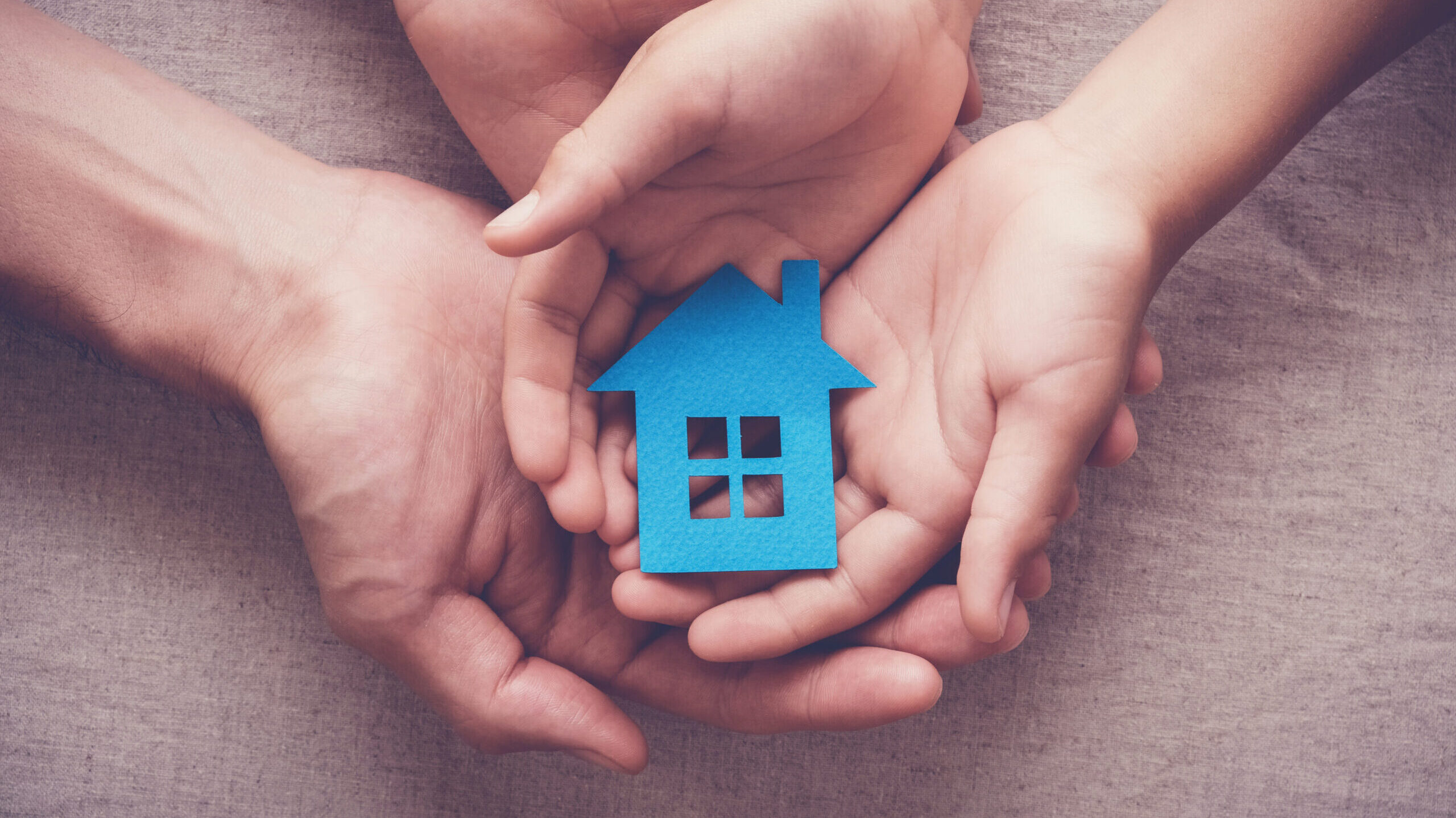 Adult and child hands holding blue paper house
