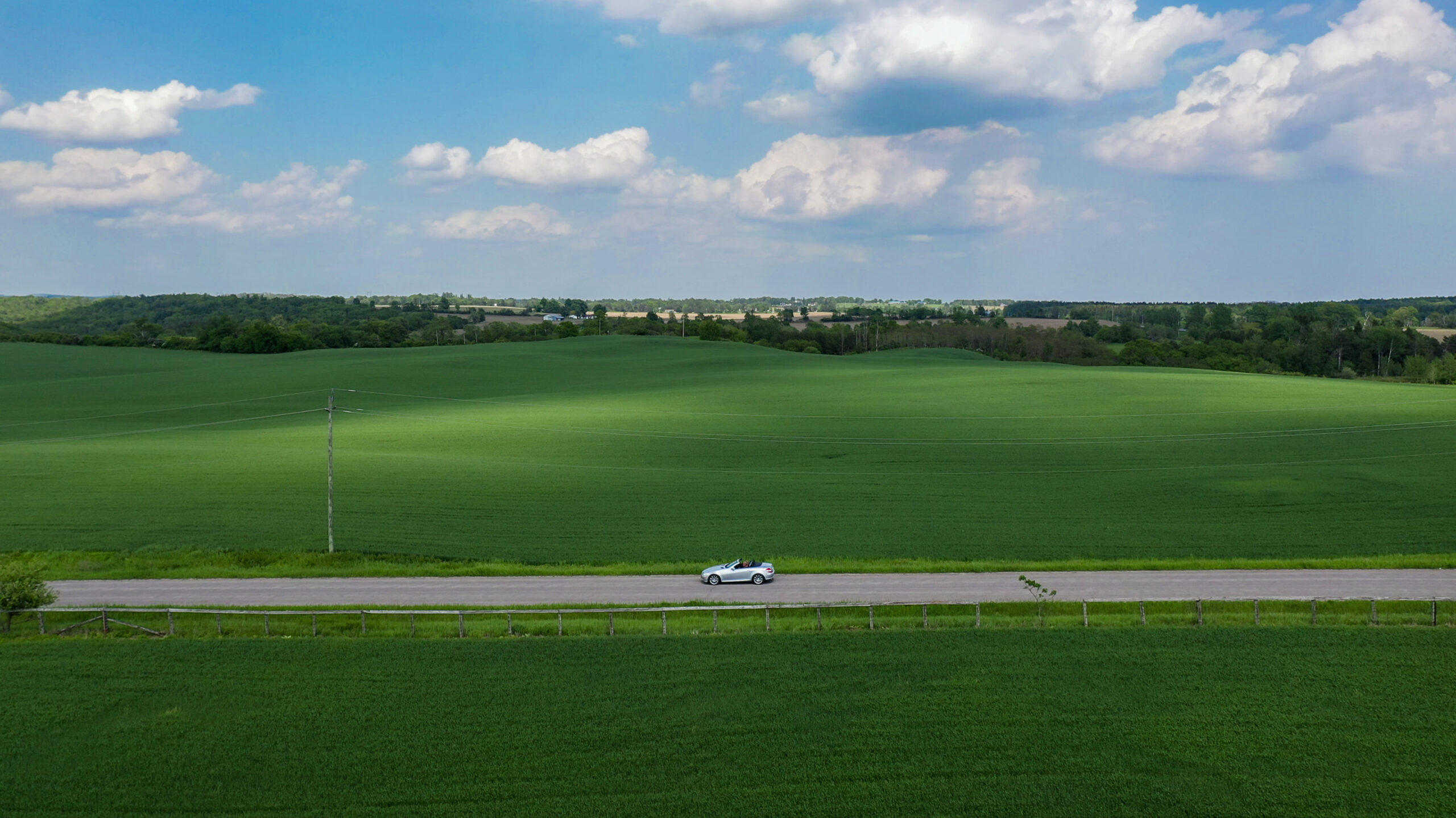 Convertible driving down Northumberland road with lush green hills in background