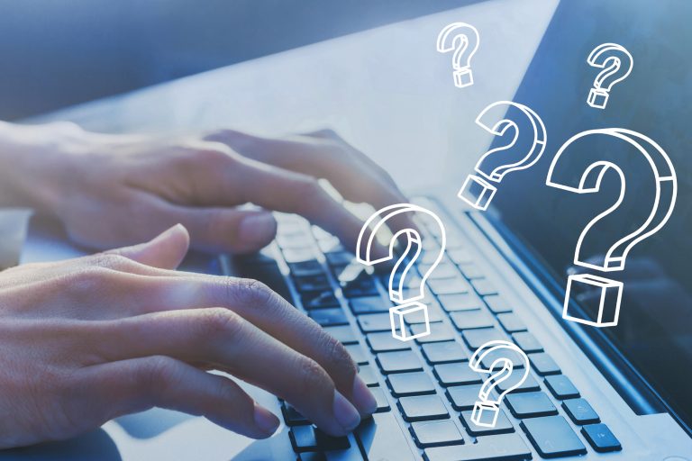 Someone typing on laptop keyboard with question marks drawn above