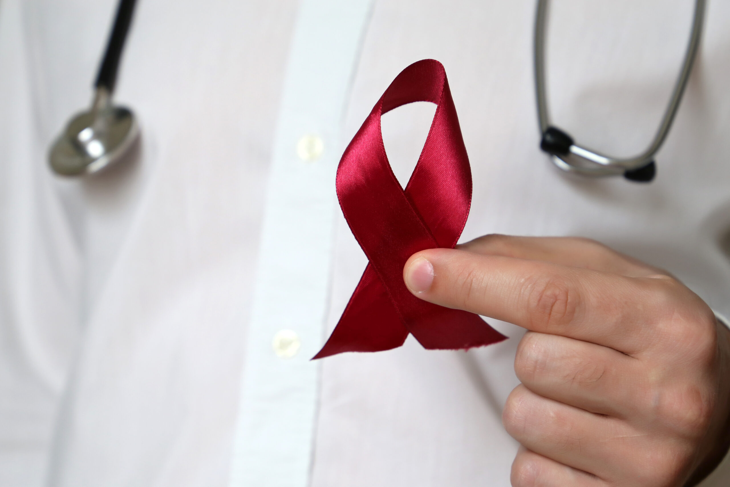 Person with a stethoscope around their neck holding up a red awareness ribbon.