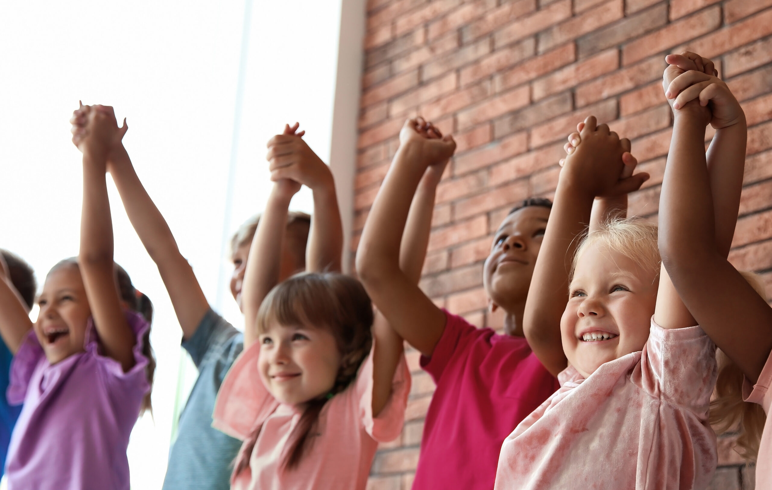 Children stand hand in hand smiling, as they lift their linked hands in the air
